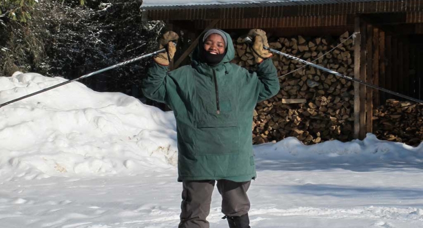 a person wearing snow gear stands on snowy ground and raises ski poles in the air